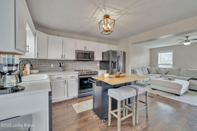 kitchen with a sink, white cabinets, open floor plan, light countertops, and appliances with stainless steel finishes