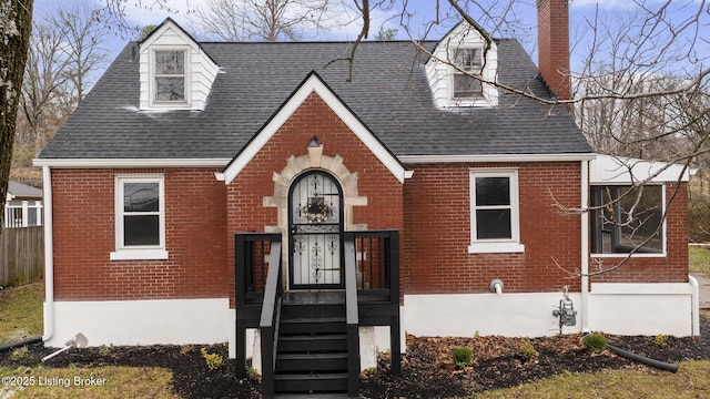 view of front facade with a shingled roof, a chimney, fence, and brick siding