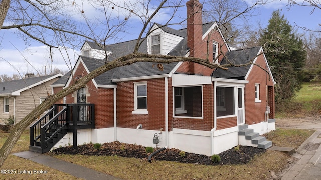 view of front facade featuring a sunroom, brick siding, a chimney, and roof with shingles