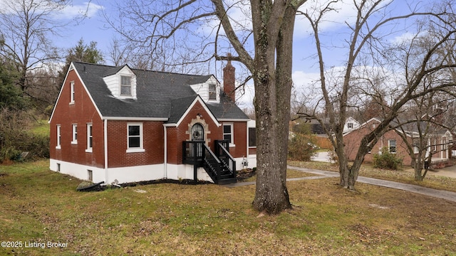 view of front facade featuring brick siding, a chimney, a front lawn, and roof with shingles