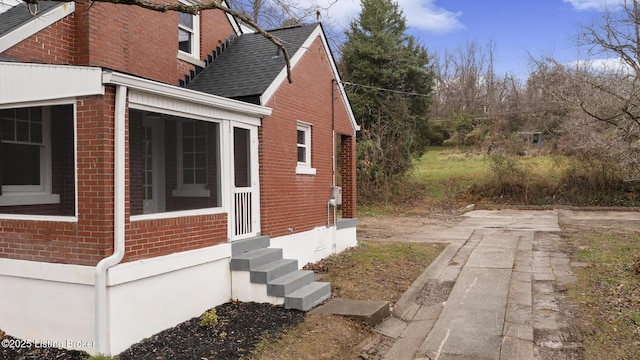 view of home's exterior with entry steps, a sunroom, brick siding, and roof with shingles