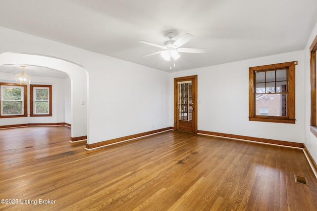 spare room featuring baseboards, visible vents, arched walkways, and wood finished floors