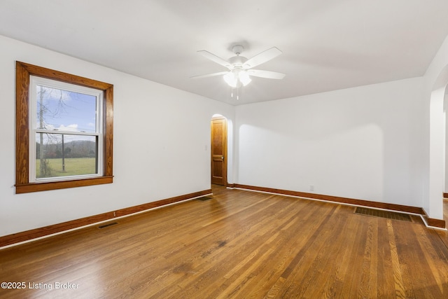 empty room featuring arched walkways, visible vents, baseboards, and wood finished floors