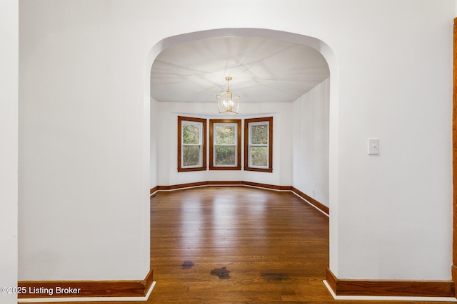 unfurnished room featuring arched walkways, a chandelier, dark wood finished floors, and baseboards