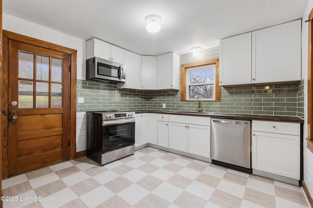 kitchen with light floors, appliances with stainless steel finishes, dark countertops, and a sink