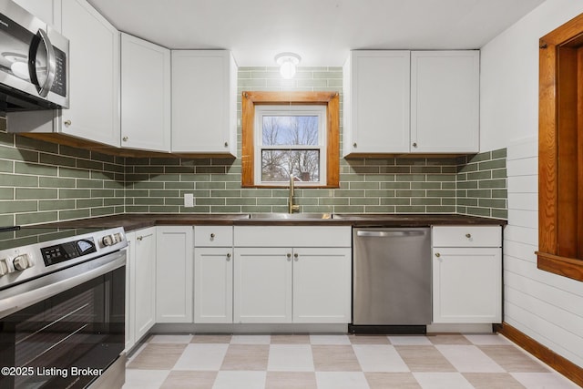 kitchen with a sink, white cabinetry, appliances with stainless steel finishes, light floors, and dark countertops