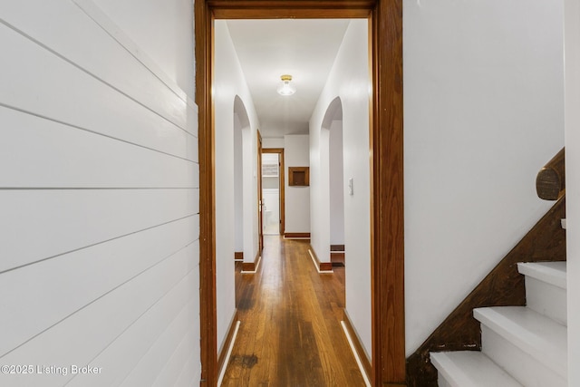 hall featuring stairway, baseboards, arched walkways, and wood finished floors