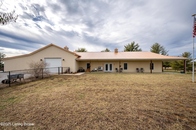 rear view of property featuring a garage, french doors, metal roof, fence, and a yard