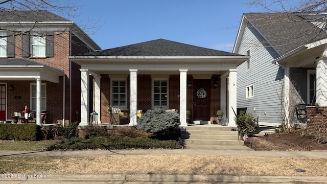 view of front of house featuring covered porch, a shingled roof, and brick siding