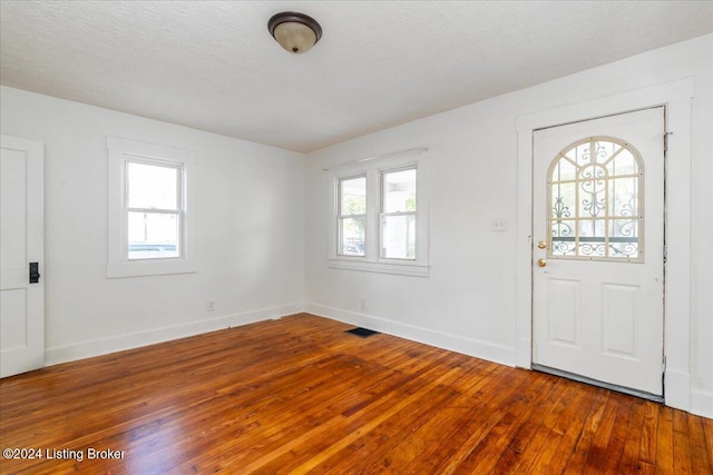 foyer entrance featuring baseboards, wood-type flooring, visible vents, and a textured ceiling