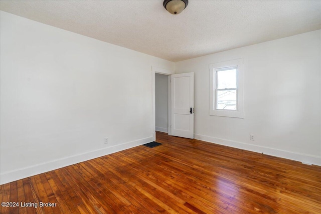 spare room featuring visible vents, baseboards, a textured ceiling, and hardwood / wood-style floors