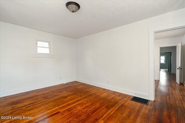 unfurnished room with wood-type flooring, visible vents, a textured ceiling, and baseboards