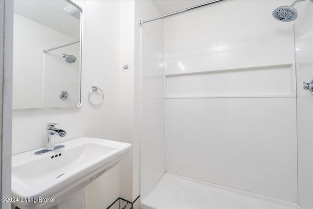 bathroom with tiled shower and a sink