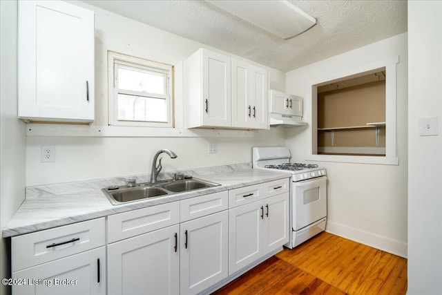 kitchen featuring under cabinet range hood, a sink, white cabinets, light countertops, and white gas range