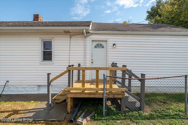 doorway to property featuring a deck, a shingled roof, a chimney, and fence