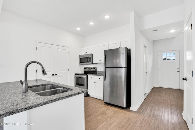 kitchen featuring stainless steel appliances, white cabinets, a sink, and dark stone countertops