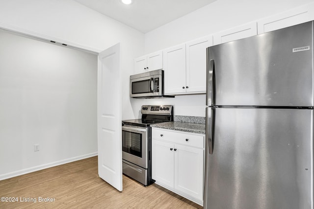 kitchen with white cabinetry, baseboards, appliances with stainless steel finishes, light wood-type flooring, and dark stone countertops