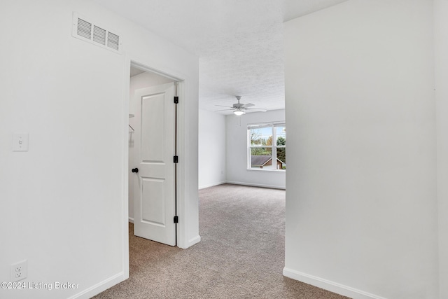 hall featuring baseboards, visible vents, a textured ceiling, and light colored carpet