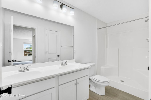 bathroom with double vanity, toilet, walk in shower, and a sink