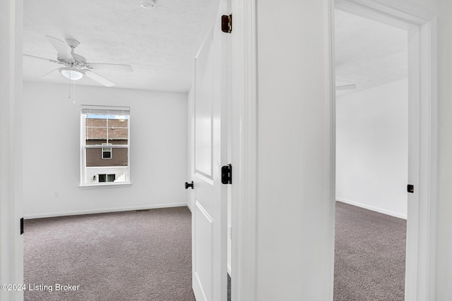 carpeted empty room with ceiling fan, baseboards, and a textured ceiling