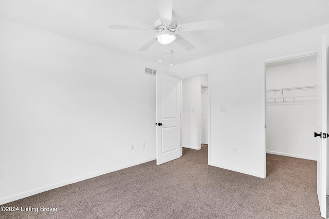 unfurnished bedroom with dark colored carpet, a walk in closet, visible vents, and baseboards