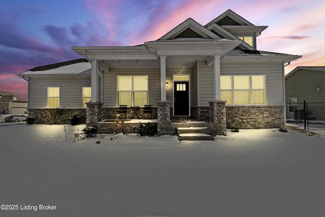 craftsman house with stone siding, covered porch, and fence