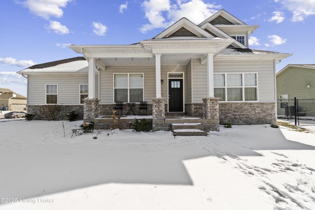 view of front facade with stone siding, covered porch, and fence