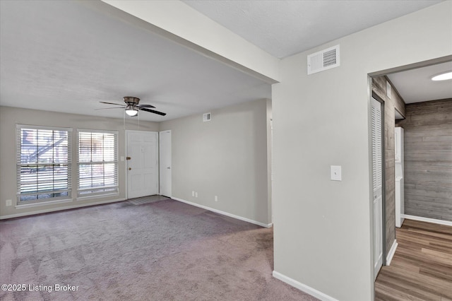 carpeted spare room with visible vents, baseboards, wood walls, and a ceiling fan