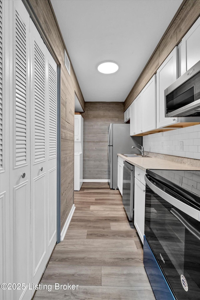 kitchen featuring white cabinetry, stainless steel appliances, light wood-style floors, wood walls, and light countertops