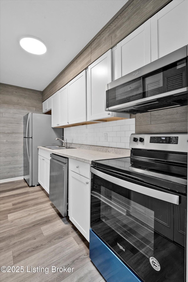 kitchen featuring light wood finished floors, decorative backsplash, white cabinets, and appliances with stainless steel finishes