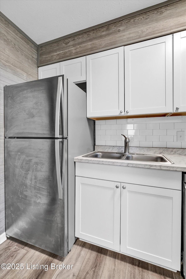 kitchen featuring a sink, light wood-type flooring, white cabinetry, and freestanding refrigerator