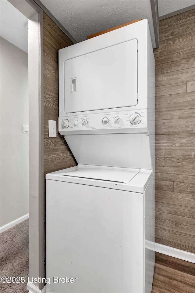 washroom featuring stacked washer / dryer, baseboards, wood walls, dark carpet, and laundry area