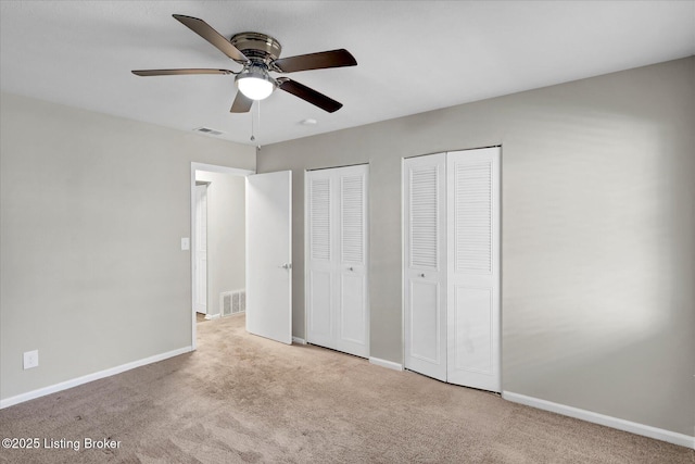 unfurnished bedroom with baseboards, visible vents, and two closets