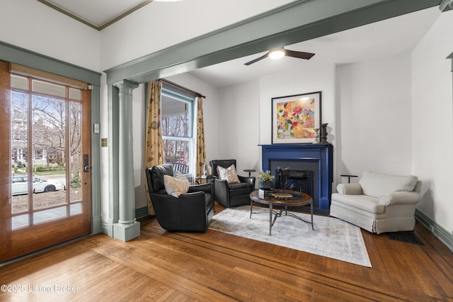 living area featuring a fireplace, decorative columns, light wood-style floors, ceiling fan, and baseboards