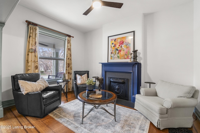 sitting room featuring a fireplace with flush hearth, ceiling fan, and wood finished floors