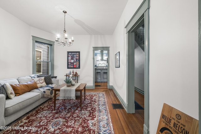 living area with baseboards, visible vents, an inviting chandelier, and wood finished floors