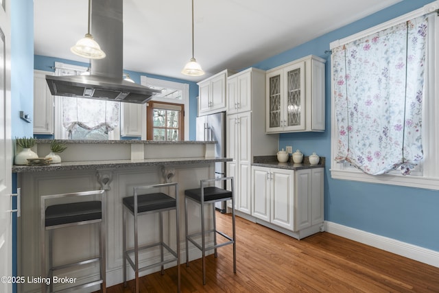 kitchen featuring white cabinets, a breakfast bar, glass insert cabinets, and island range hood