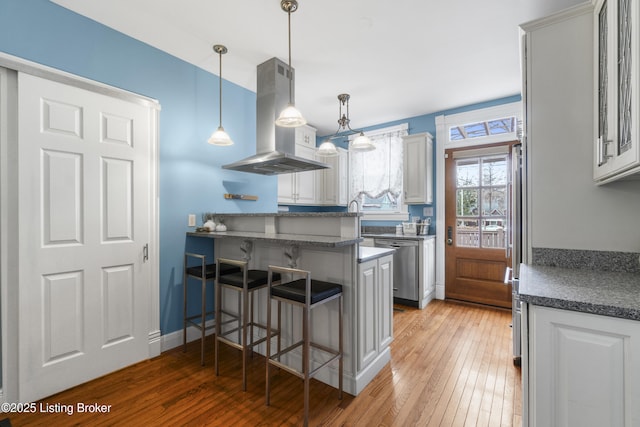 kitchen with island range hood, dishwasher, a breakfast bar, decorative light fixtures, and a peninsula