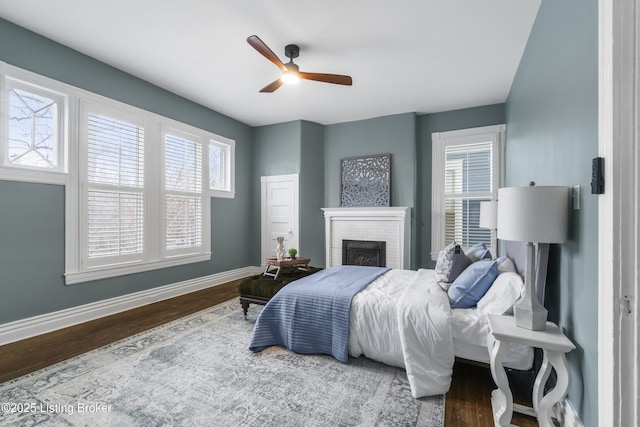 bedroom featuring a brick fireplace, ceiling fan, baseboards, and wood finished floors