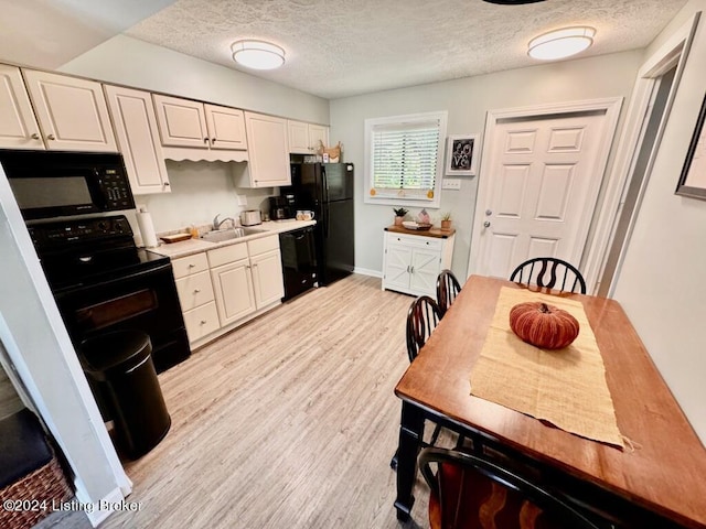 kitchen with light wood-style flooring, light countertops, a textured ceiling, black appliances, and a sink