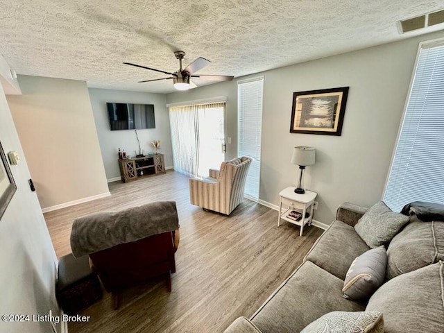 living room featuring visible vents, baseboards, light wood-style flooring, ceiling fan, and a textured ceiling