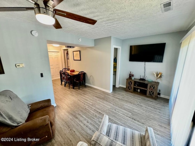 living area featuring a textured ceiling, a ceiling fan, light wood-style flooring, and baseboards