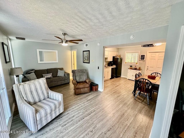 living room featuring visible vents, light wood-style floors, a ceiling fan, a textured ceiling, and baseboards