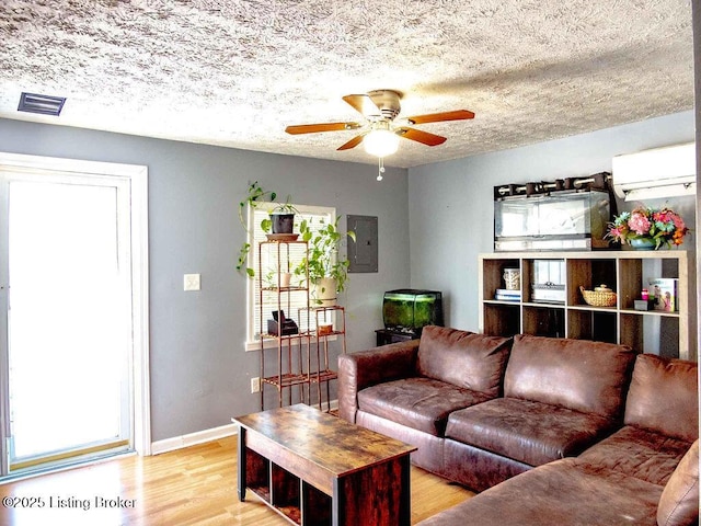 living room with light wood-style flooring, a ceiling fan, visible vents, electric panel, and a wall mounted air conditioner