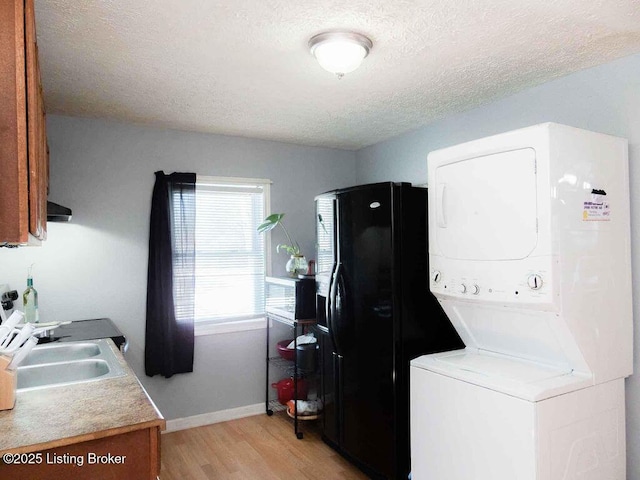 laundry room featuring stacked washer / drying machine, a textured ceiling, light wood-type flooring, laundry area, and baseboards