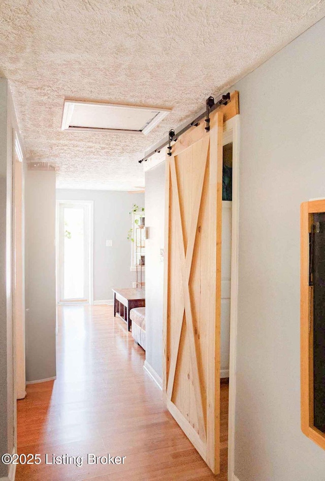 corridor featuring a barn door, a textured ceiling, and wood finished floors