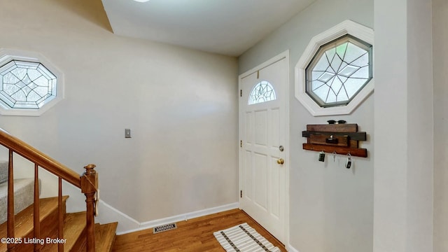 entrance foyer with stairs, visible vents, baseboards, and wood finished floors