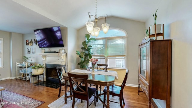 dining space with baseboards, lofted ceiling, a fireplace with flush hearth, wood finished floors, and an inviting chandelier