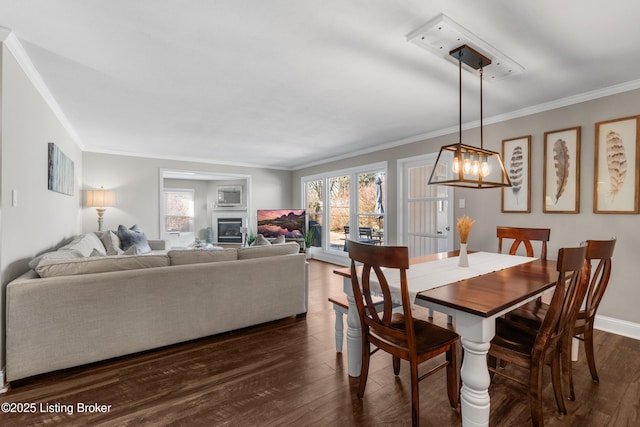 dining space featuring baseboards, dark wood finished floors, a glass covered fireplace, ornamental molding, and an inviting chandelier