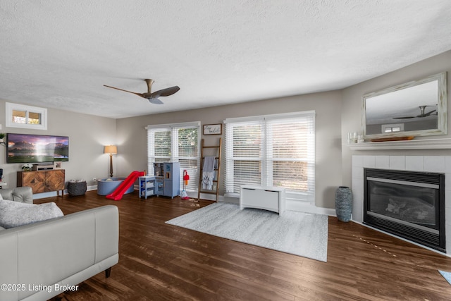 living room featuring a textured ceiling, a fireplace, dark wood finished floors, and a ceiling fan